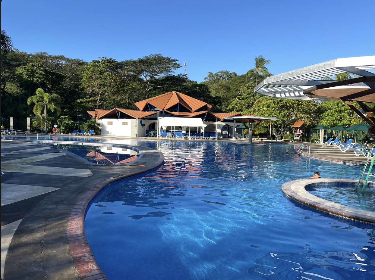 The club's main pool at water level, with buildings, palms and forest behind