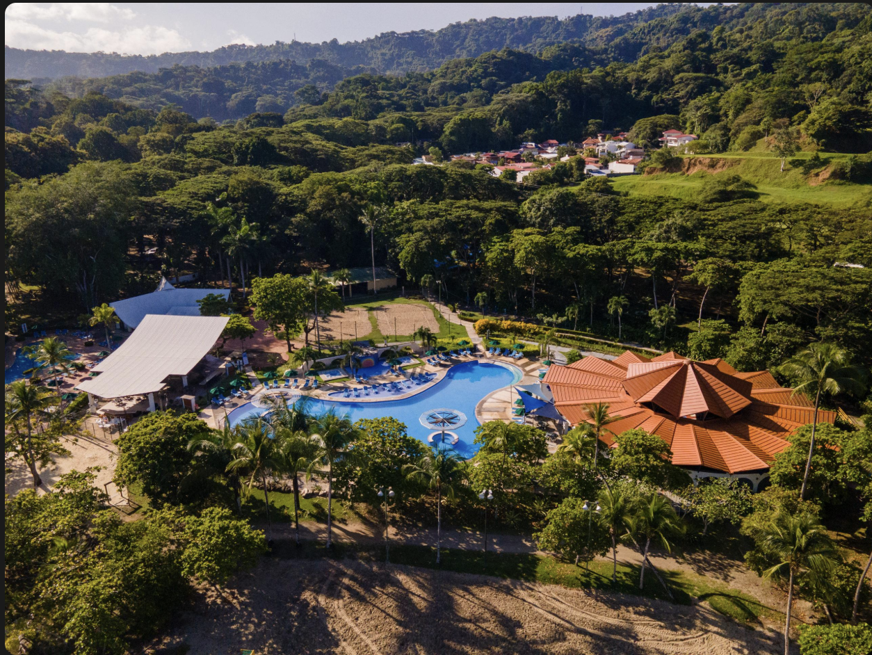 Aerial view of the club's pools and thatched roofs among the trees