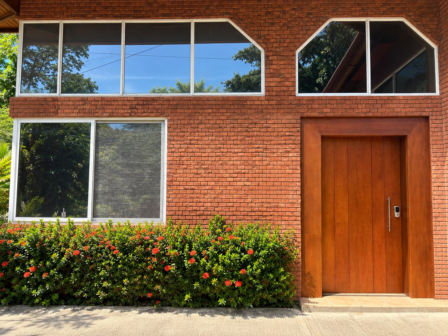 Casa Coral exterior: two-storey brick home with white-framed windows, wooden front door and a flowering hedge
